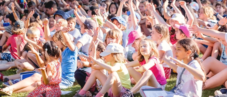 Viele Kinder sitzen gemeinsam bei einer Veranstaltung im Freien.