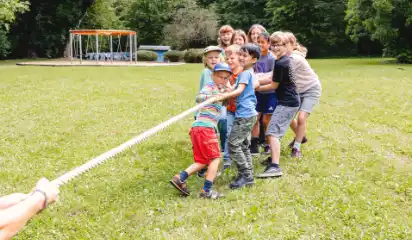 Kinder und ein Betreuer ziehen gemeinsam an einem Seil.