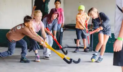 Kinder spielen gemeinsam Hockey in einer Halle.