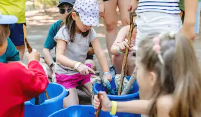 Kinder und Betreuerin schöpfen Wasser bei einem Spiel im Freien.