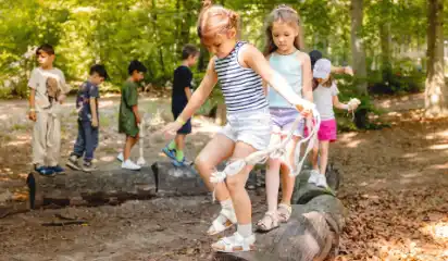 Kinder balancieren auf einem Baumstamm im Wald.