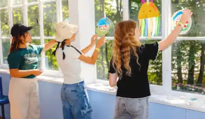 Kinder bemalen gemeinsam bunte Masken am Fenster.