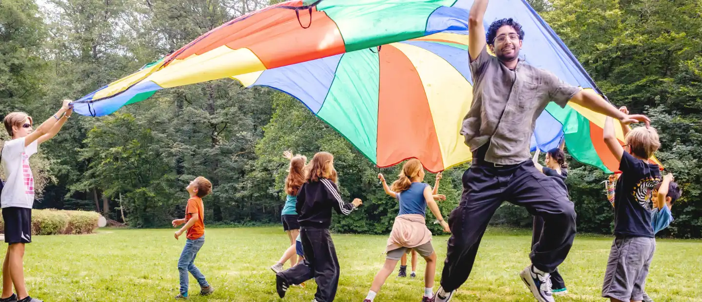 Kinder spielen mit einem bunten Schwungtuch auf einer Wiese.