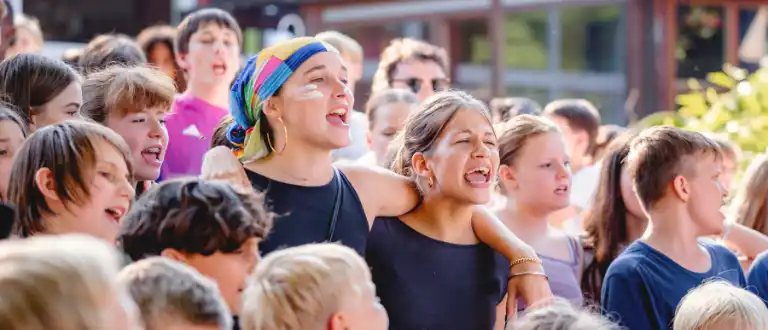 Betreuende stehen inmitten einer fröhlichen Kindergruppe.