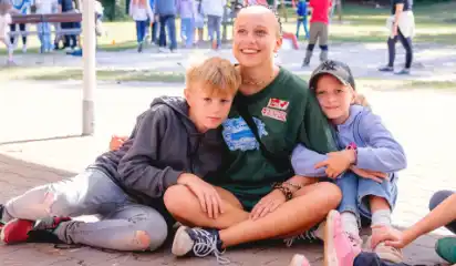 Betreuerin sitzt mit zwei Kindern auf dem Boden.