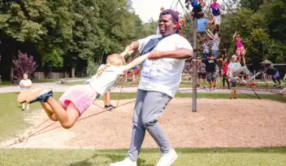 Betreuer dreht ein Kind auf einem Spielplatz im Kreis.