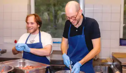 Zwei Küchenhelfer bereiten eine warme Mahlzeit vor.